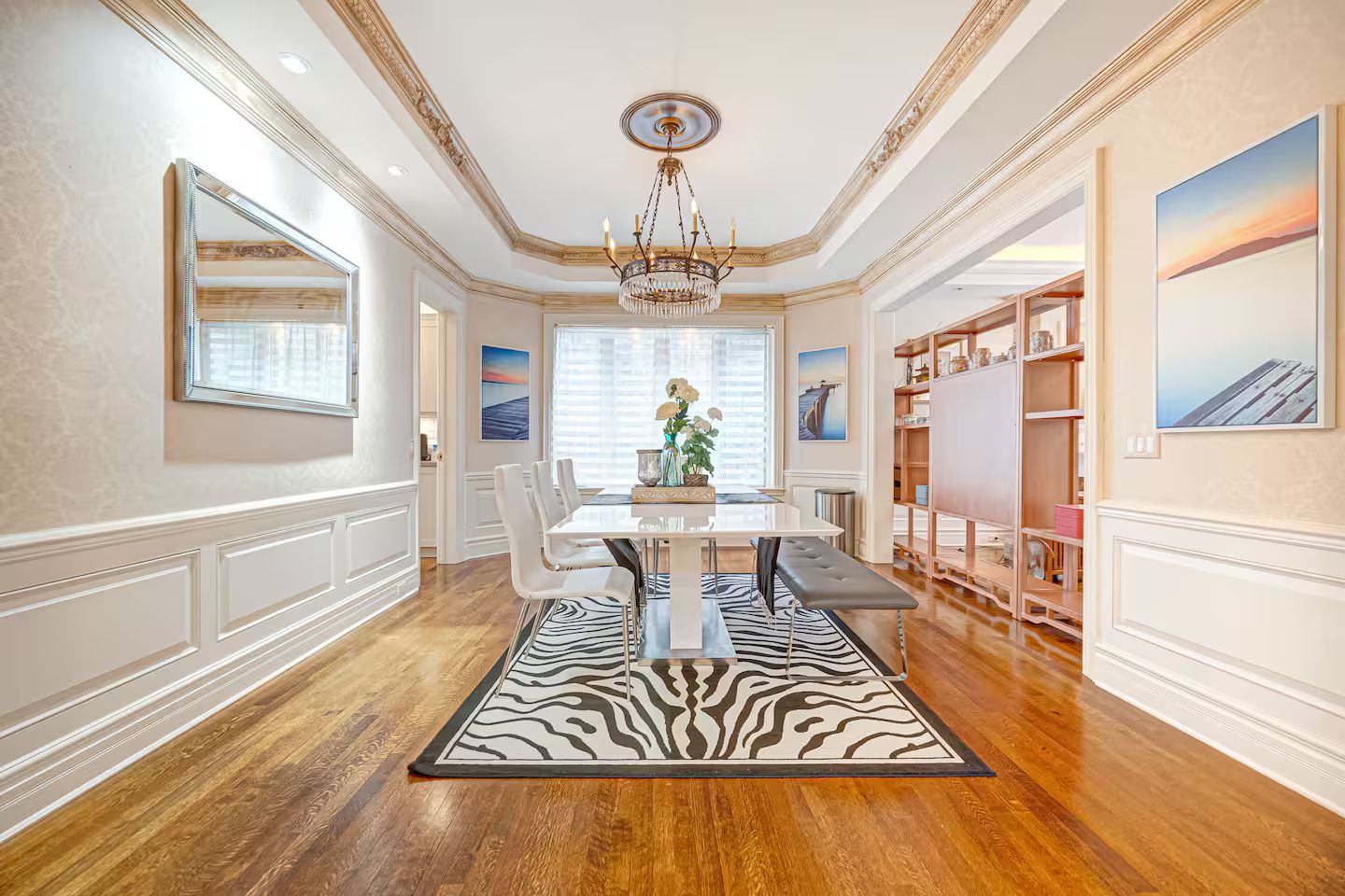 A spacious dining area with a zebra-patterned rug, a chandelier, and a view of the outdoors through large windows.