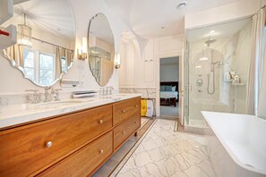 Een moderne badkamer met een grote spiegel, een houten wastafelmeubel, een badkuip en een douchehoek.