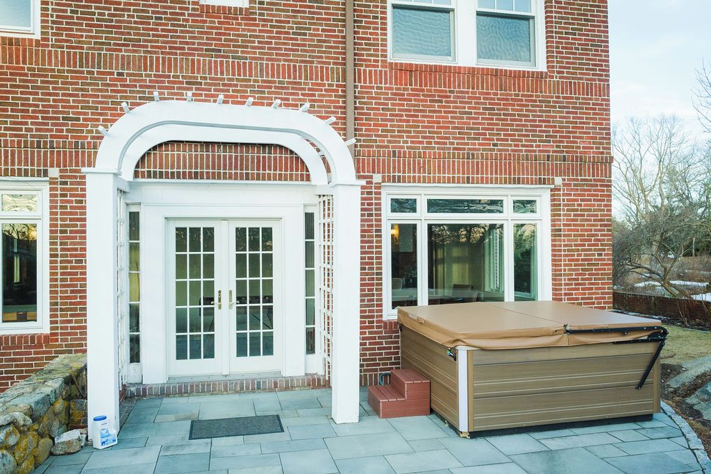 A brick house with a white arched entryway, a sliding glass door, and a covered patio area.