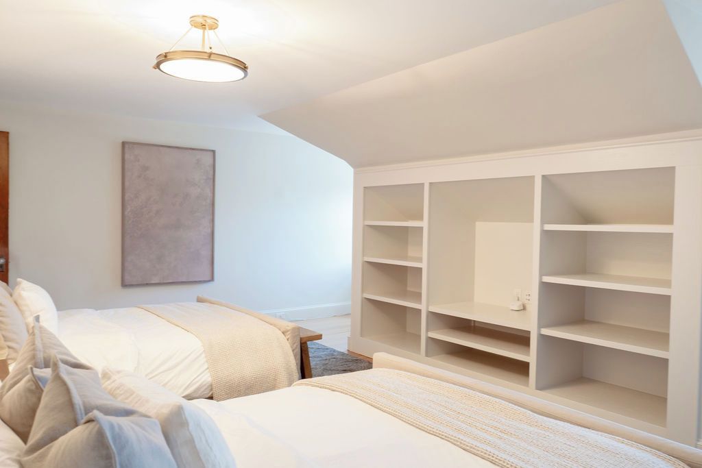 A bedroom with two beds, a large white wardrobe, and a ceiling light fixture.