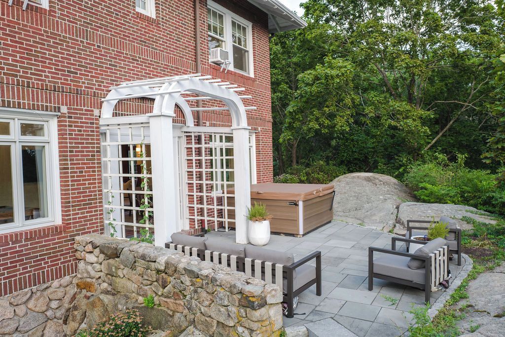 Una casa de ladrillo con un patio que cuenta con una pérgola blanca, un jacuzzi y mobiliario para exteriores.