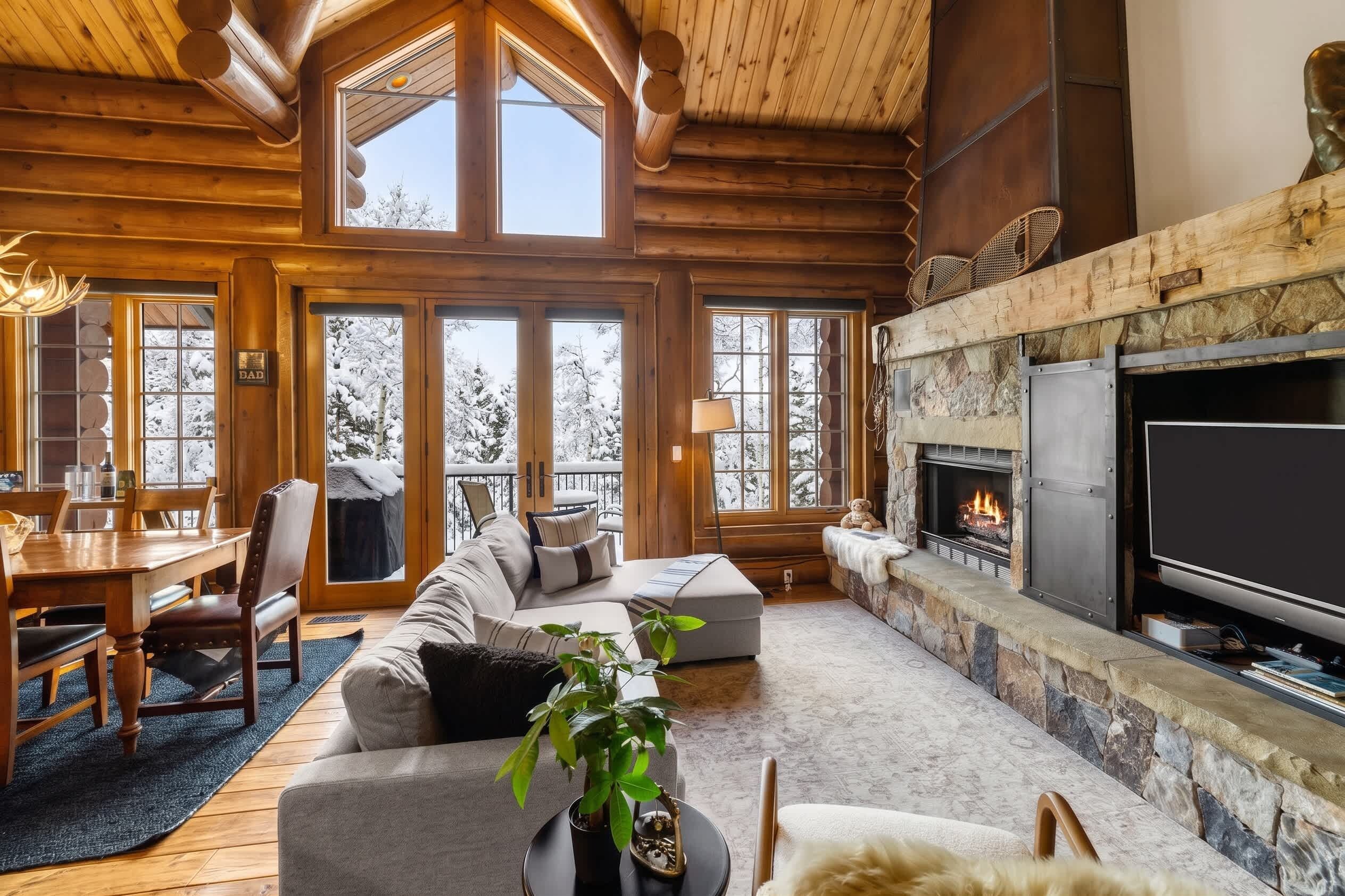 Un intérieur chaleureux de chalet en bois, avec une cheminée, de grandes fenêtres et un coin salon confortable.
