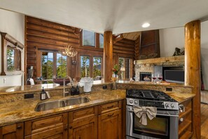 A spacious kitchen with granite countertops, wooden cabinets, a stainless steel sink, a gas stove, and a large window offering a view of the outdoors. - Mountain Village Gem|Hot Tub+Views+Ski-In/Out (Mountain Village)