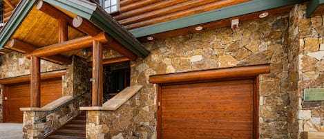 Eine Blockhütte mit Natursteinfassade, Holztüren zur Garage und einer Treppe zum Eingang.