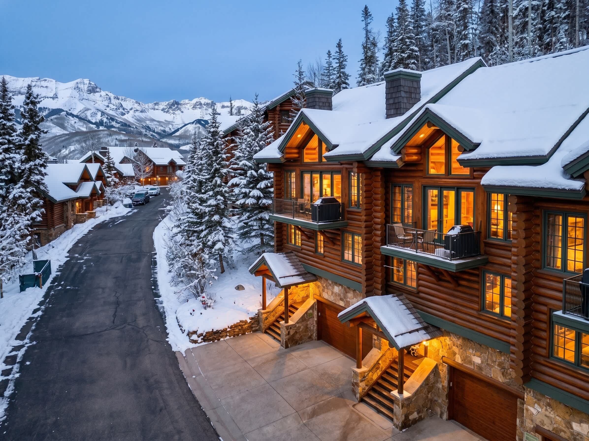 Un hôtel aménagé dans un chalet en rondins, avec une allée enneigée et une vue sur les montagnes en toile de fond.