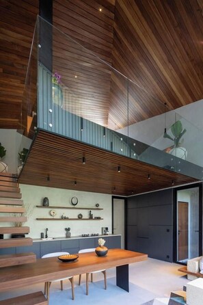 A modern interior with a wooden ceiling, a glass staircase, and a dining area with a table and chairs.