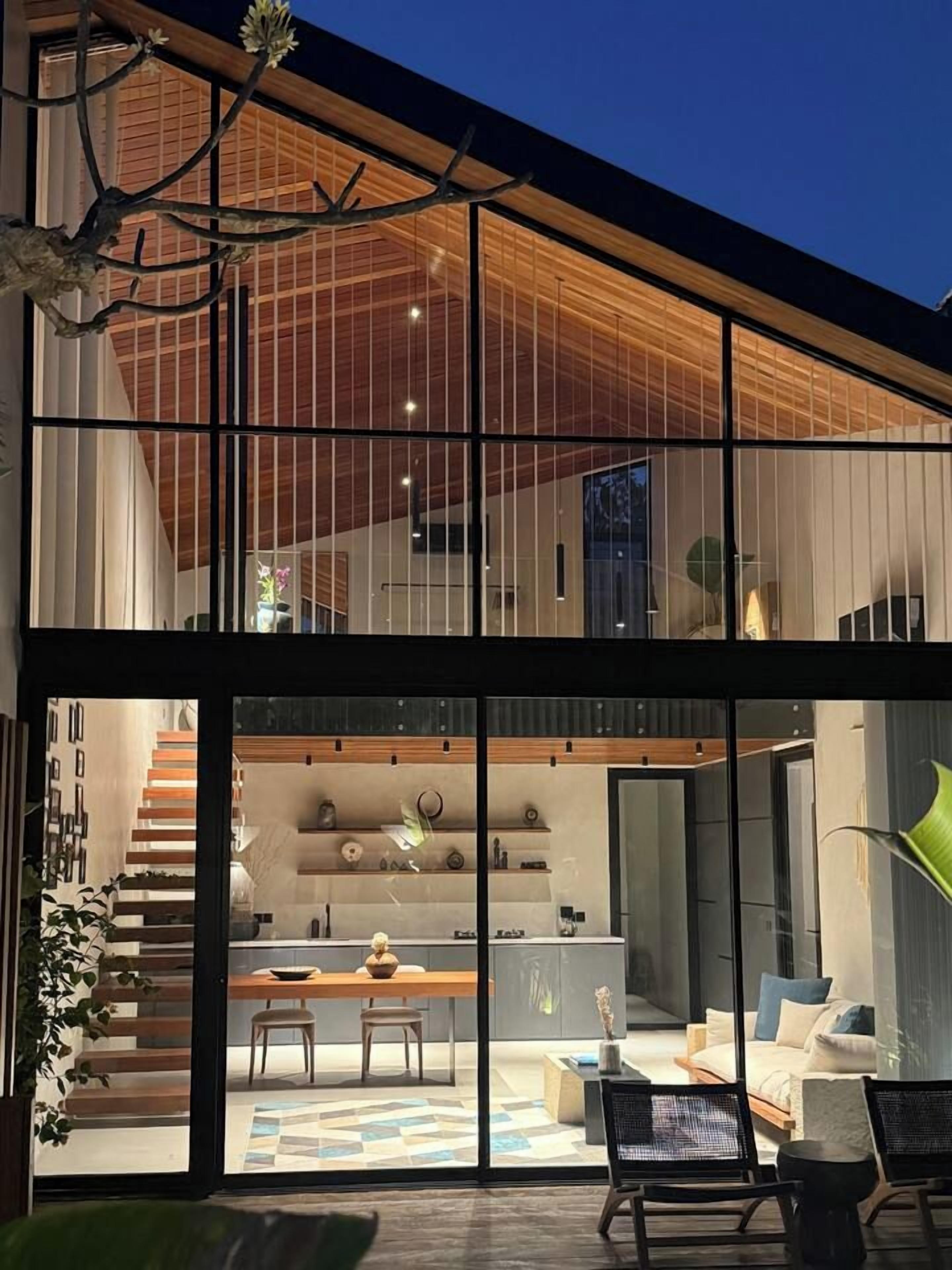 Ein modernes Haus mit einer großen Glasfassade, einer Holztreppe und einem Essbereich mit Tisch und Stühlen.