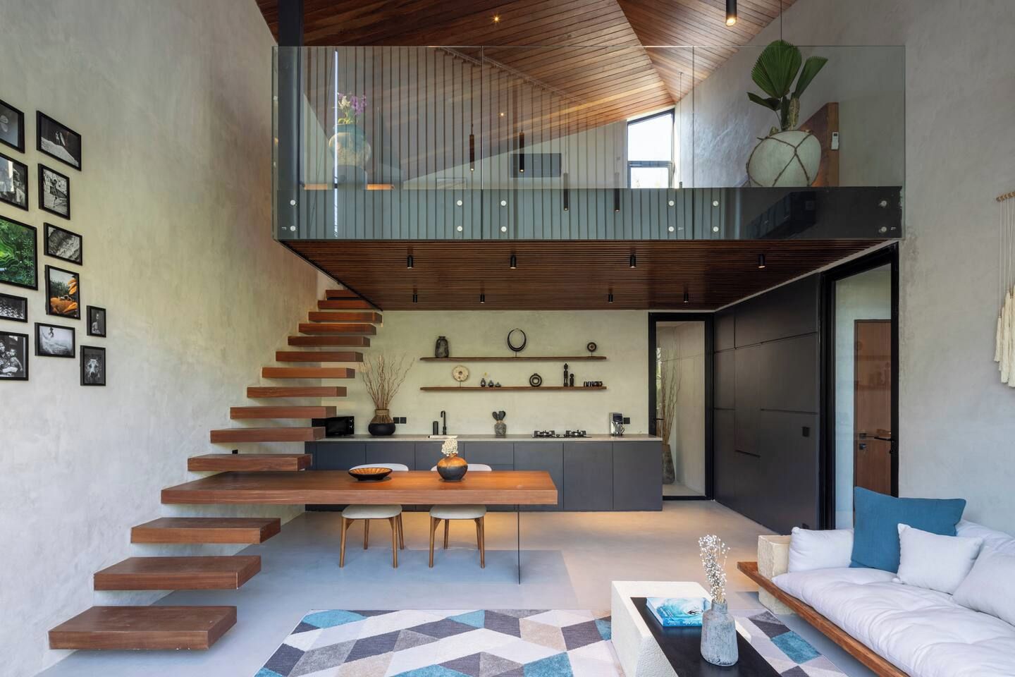 Ein modernes Interieur mit einer Treppe zu einem Schlafbereich, einer Küchenzeile und einer Sitzecke mit Sofa und Couchtisch.