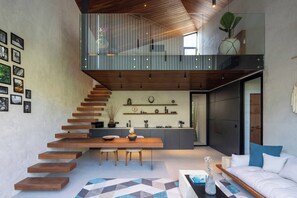 A modern interior with a staircase leading to a loft, a kitchen area, and a seating space with a sofa and coffee table.