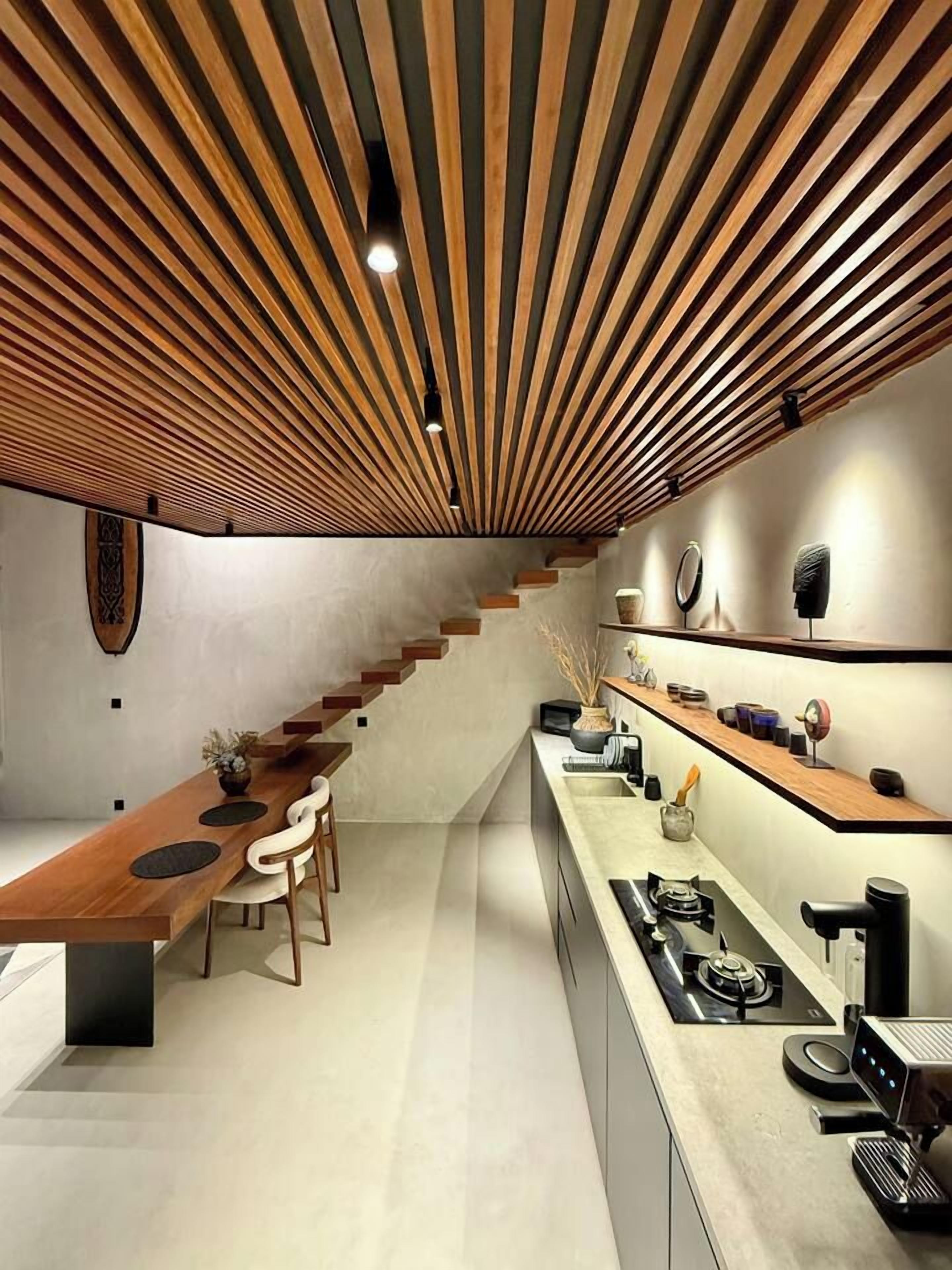 A modern kitchen with a wooden slatted ceiling, a long dining table, and a built-in stove.