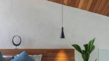 Ein modernes Schlafzimmer mit Holzbalkendecke, einem Bett mit blauen Kissen, einem Nachttisch mit Lampe und einer großen Topfpflanze.