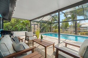 A covered outdoor area with a pool, seating, and a grill.