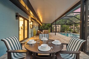 A covered outdoor dining area with a pool in the background.