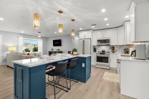 A modern kitchen with white cabinets, a central island with bar stools, and a flat-screen TV mounted above the island.