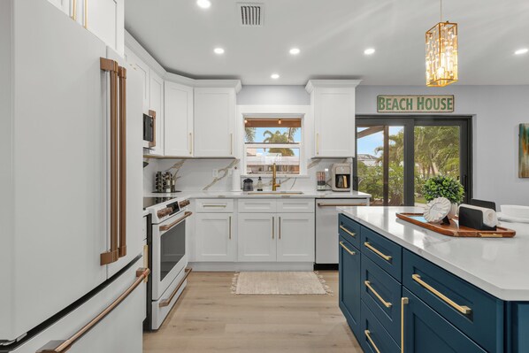 Una cocina moderna con armarios blancos, una isla central y un cartel que dice 'BEACH HOUSE'.