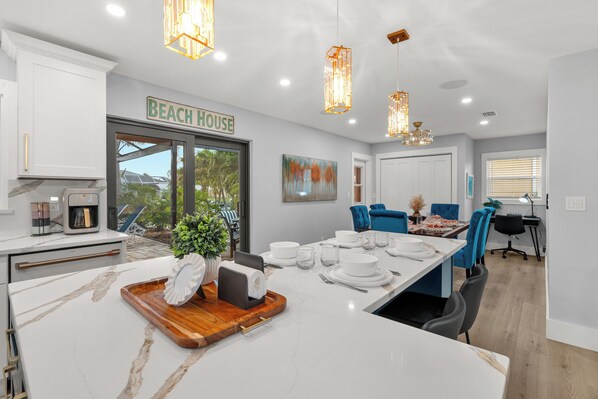 A modern kitchen with a marble countertop, a coffee machine, and a sign reading 'BEACH HOUSE'.