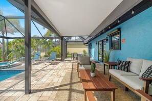 Un espacio al aire libre techado con piscina, sillones de descanso, un sofá y una mesa.
