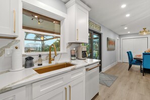 Una cocina moderna con armarios blancos, un grifo dorado y una ventana con vistas a un jardín.