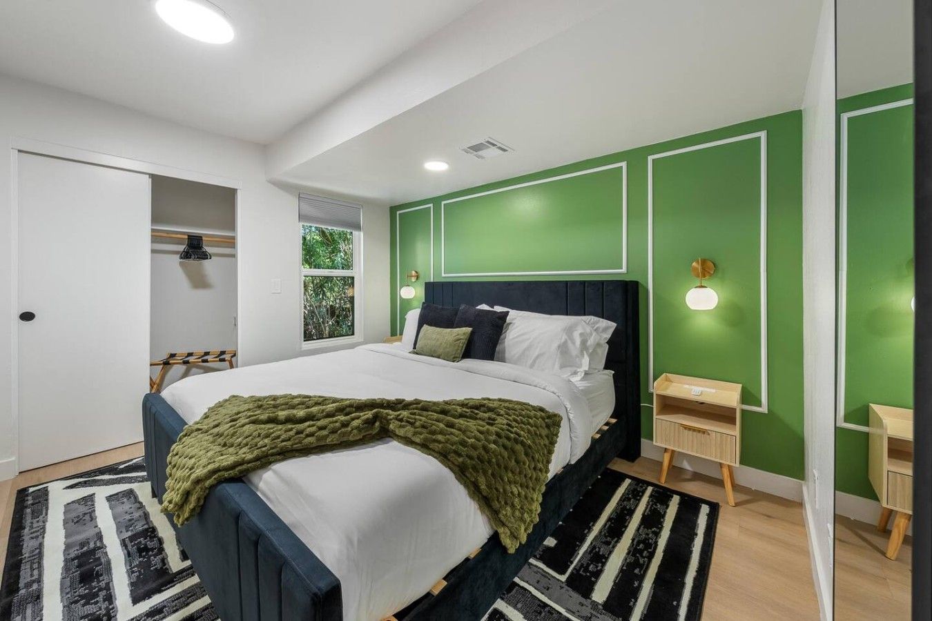 A modern bedroom with a bed, a bedside table, a wardrobe, and a window with a view of greenery.