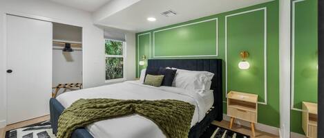 A modern bedroom with a bed, a bedside table, a wardrobe, and a window with a view of greenery.