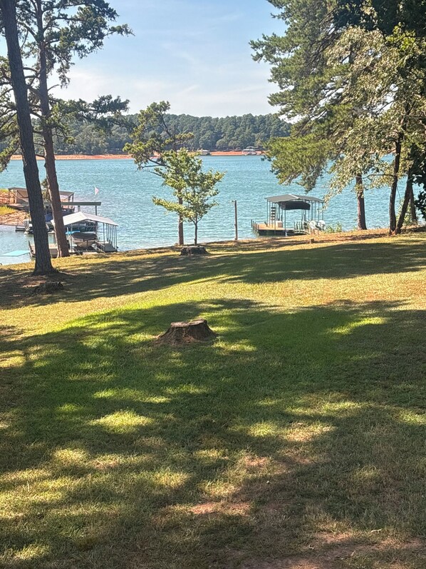 Une vue sur le lac, avec un quai, un espace de repos abrité et une zone herbeuse bordée d’arbres.