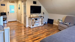 Un accogliente soggiorno con pavimento in legno, una ventola a soffitto, una TV a schermo piatto e un'area salotto confortevole.