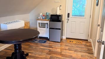 Een compacte keuken met een eettafel, een koelkast, een magnetron en een koffiezetapparaat.
