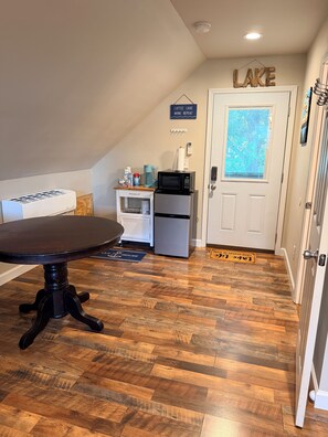 A compact kitchen with a dining table, a refrigerator, a microwave, and a coffee maker.