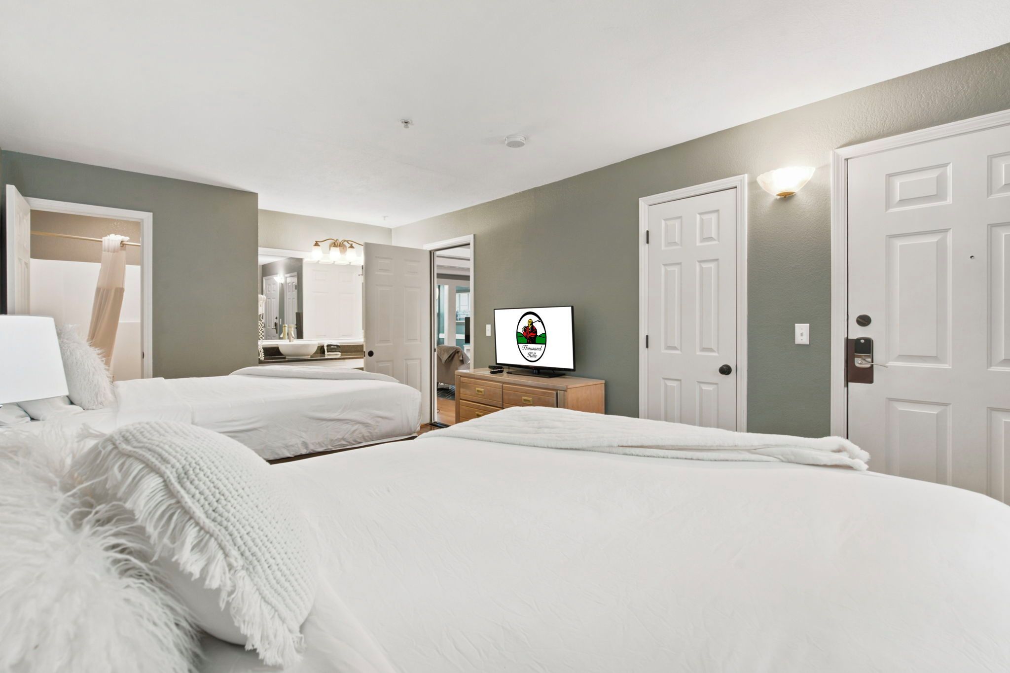 A hotel room with two beds, a vanity with a mirror, a television, and a door with a lock.