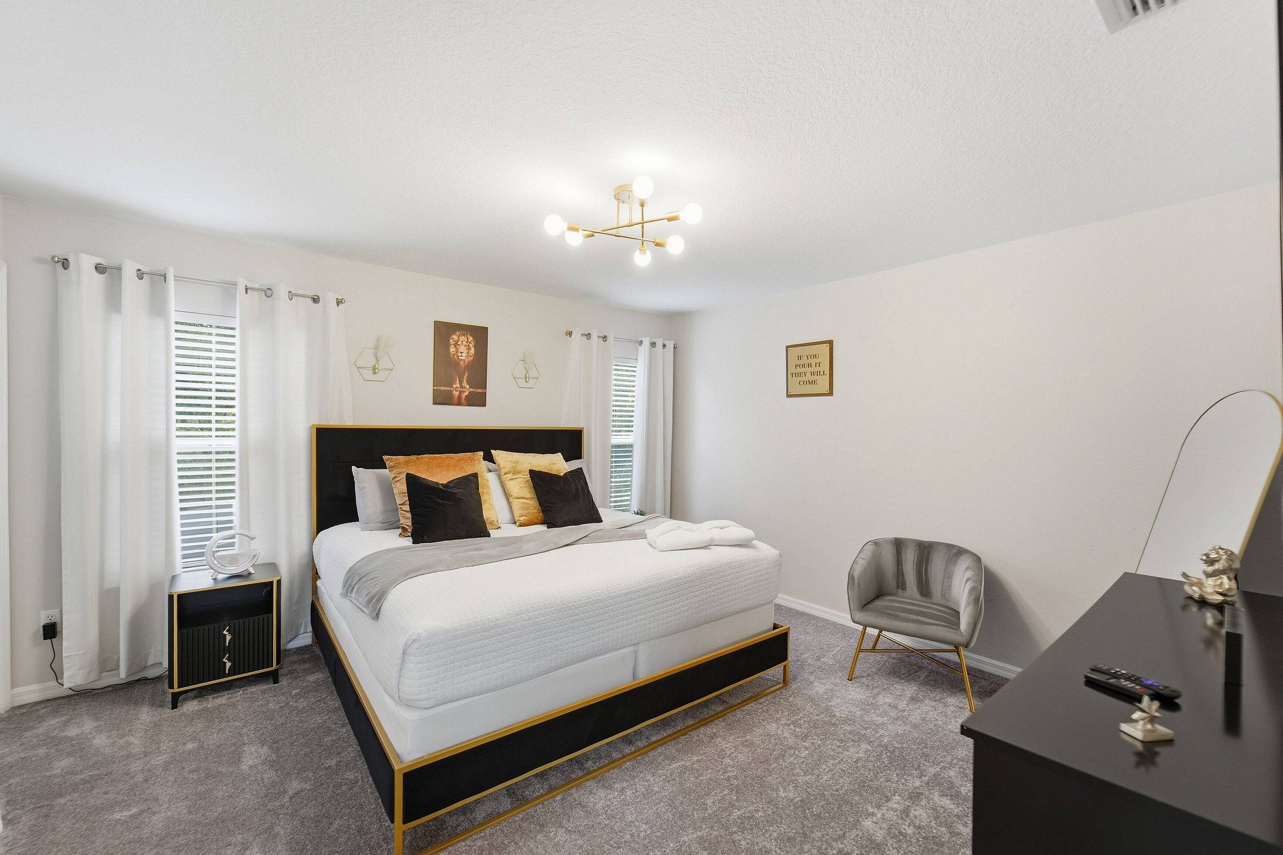 A bedroom with a bed, bedside tables, a chair, a desk, and a wall-mounted light fixture.