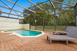 An outdoor swimming pool with a glass enclosure, surrounded by a brick patio and equipped with lounge chairs. - 4BR Bella Vida Home Near Disney for 11 Guests (Kissimmee)