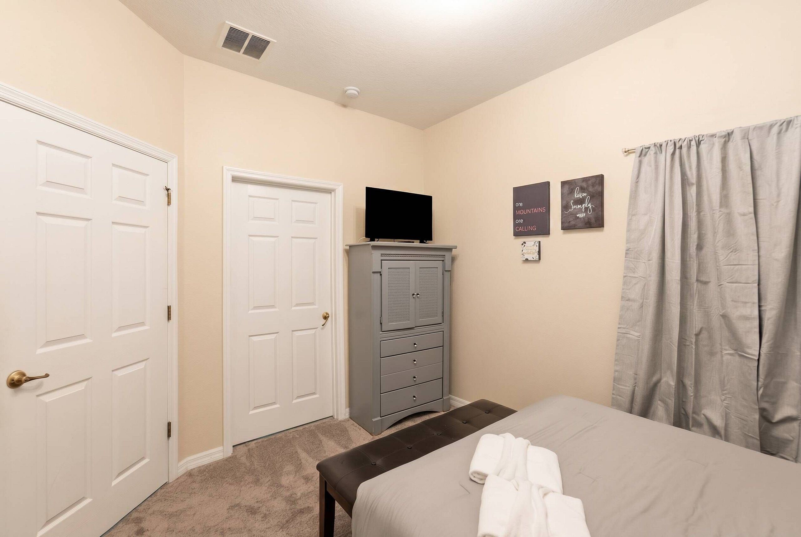 Une chambre à coucher avec un lit, une commode, un téléviseur posé sur la commode et une porte.