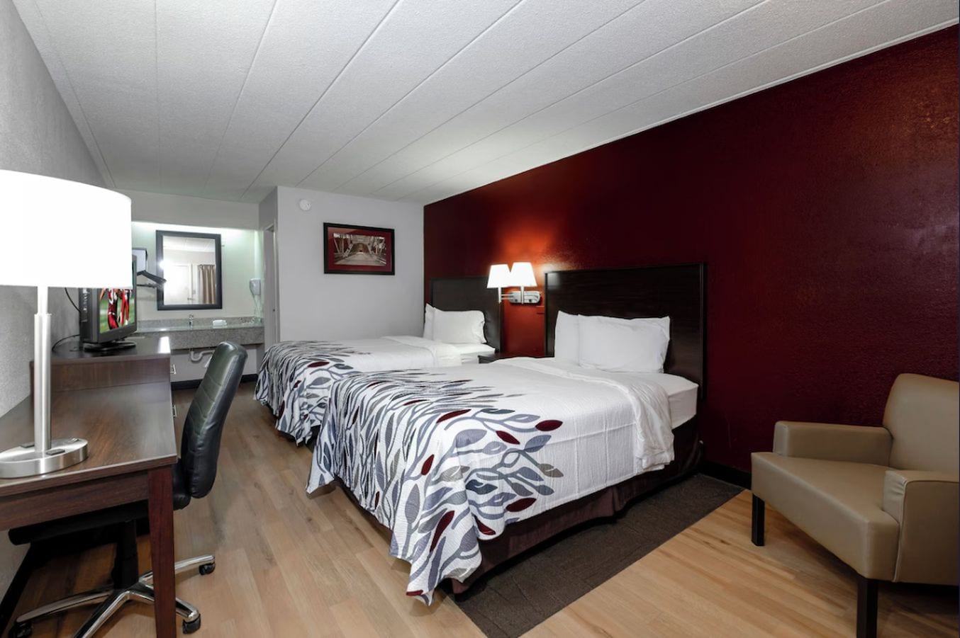 Habitación de hotel con dos camas, un escritorio, una silla y un televisor.