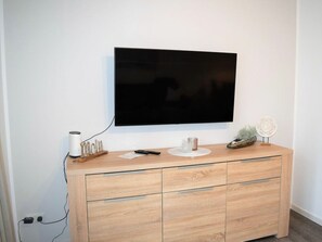 Ein modernes Wohnzimmer mit einem wandmontierten Flachbildfernseher, einer Holzkassette mit Schubladen und einem kleinen dekorativen Gegenstand darauf.