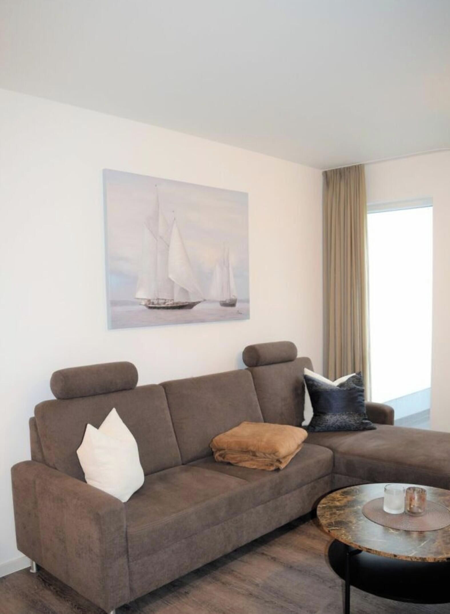 A modern living room with a brown sofa, a round coffee table, and a painting of sailboats on the wall.
