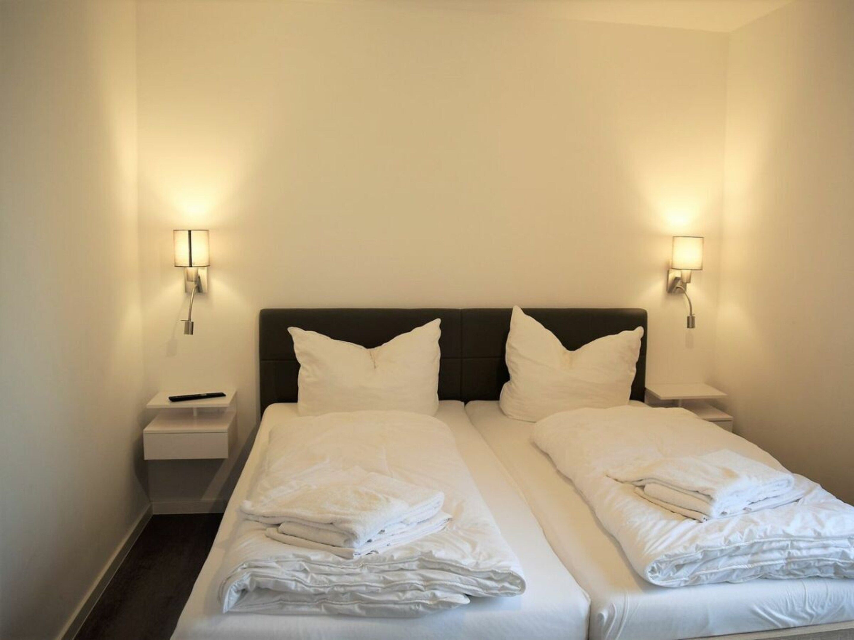 Una habitación de hotel con una cama doble, dos mesitas de noche y dos lámparas de pared.