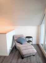 A minimalist room with a single bed, a small round table, and a large window.