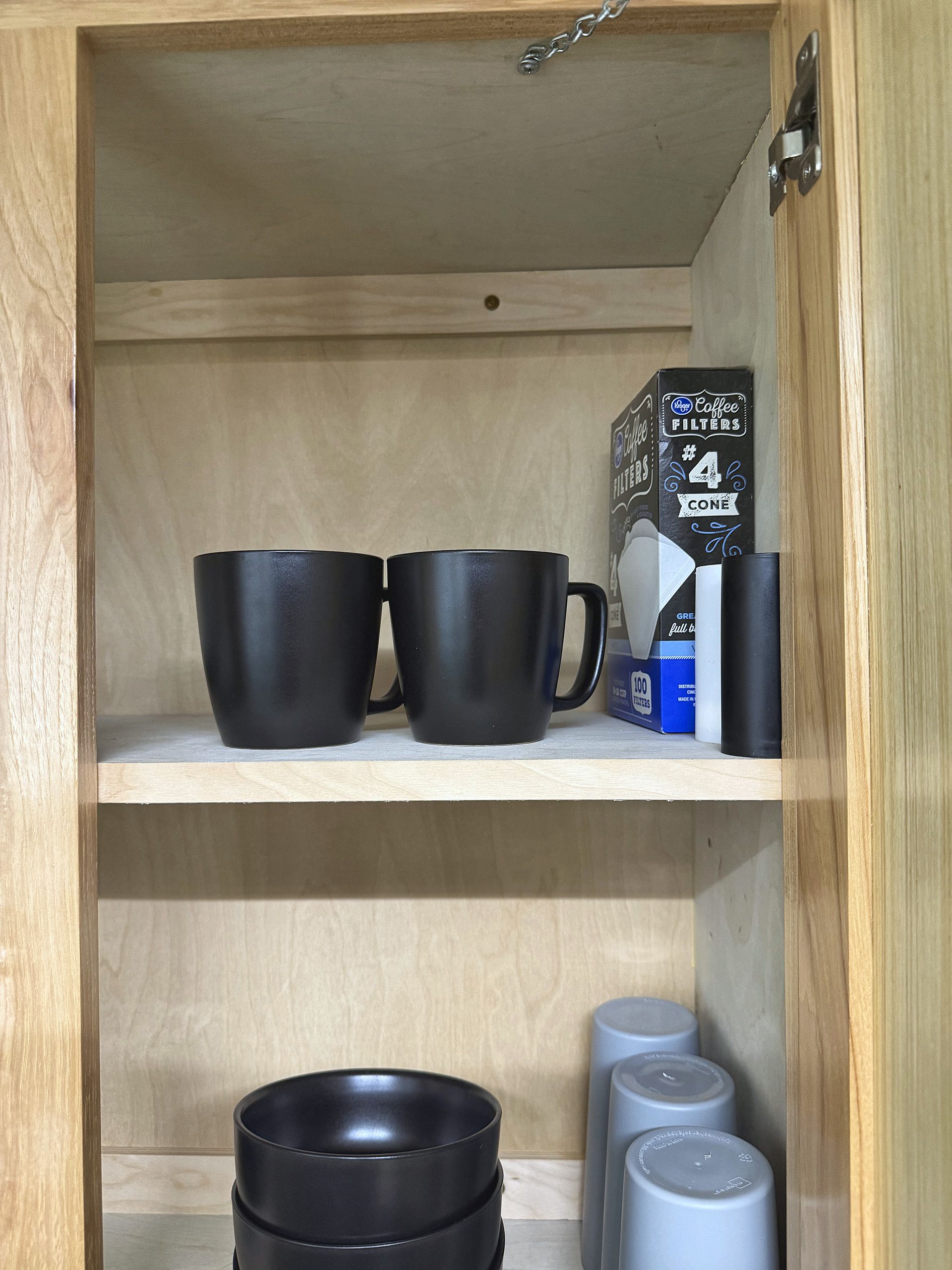 A wooden cabinet with black mugs and a coffee filter box.