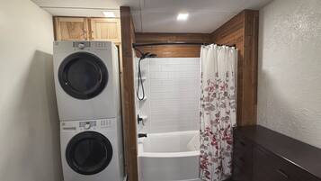 A compact bathroom with a washing machine, a bathtub, and a shower curtain.