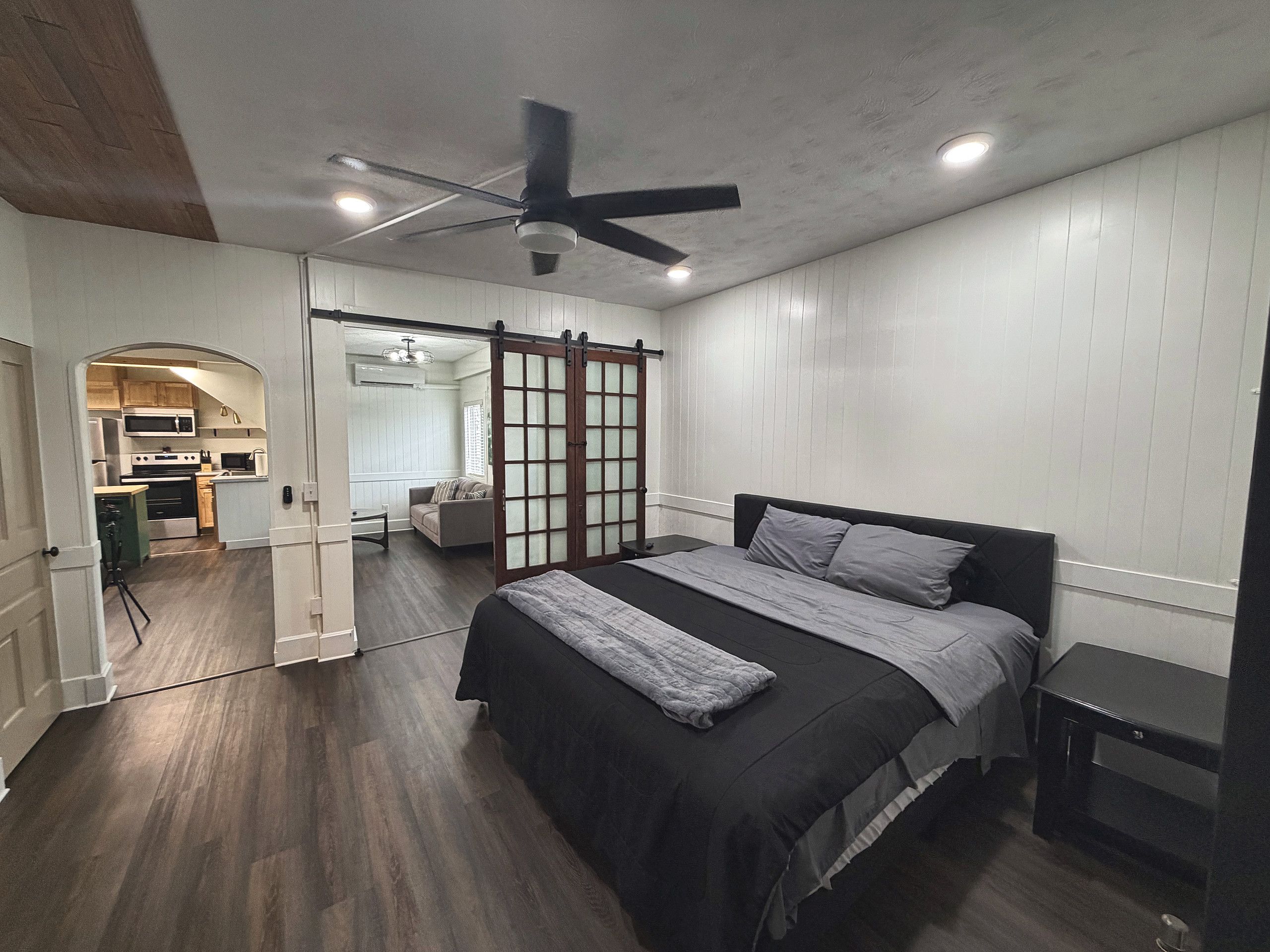 A bedroom with a bed, a nightstand, a ceiling fan, and a sliding door leading to a bathroom.