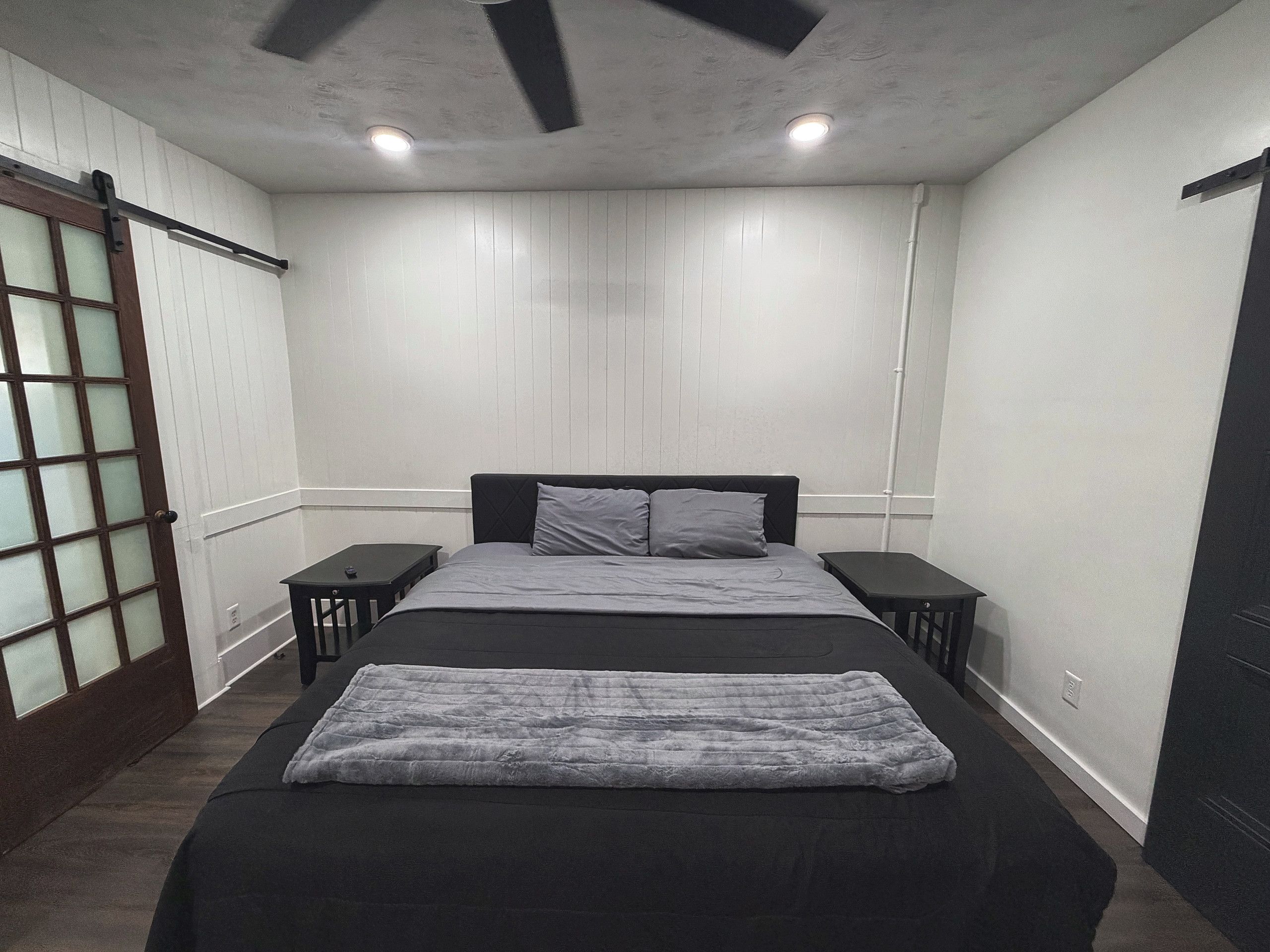 A bedroom with a bed, two bedside tables, a ceiling fan, and a sliding door with frosted glass panels.