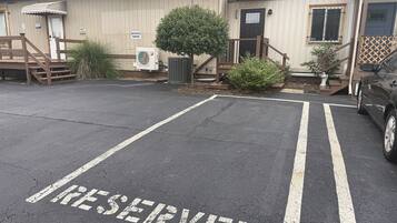 Un área de estacionamiento con la palabra 'RESERVED' pintada en el suelo, un edificio con una puerta y escalones, y un coche estacionado al lado.