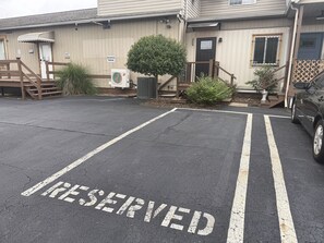 Een parkeerplaats met 'RESERVED' op de grond geschilderd, een gebouw met een deur en trap, en een auto aan de zijkant geparkeerd.