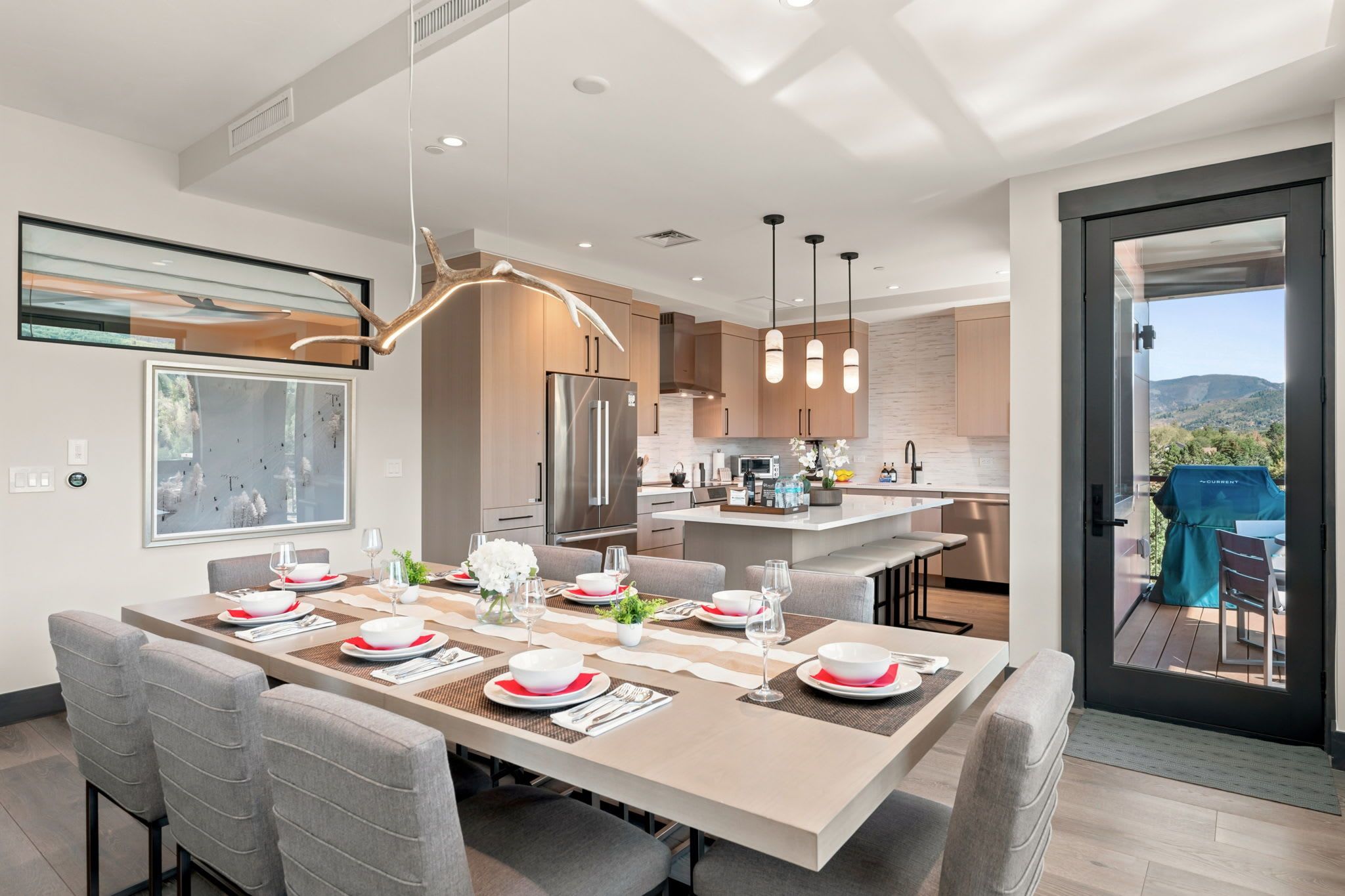 A modern kitchen with a dining area, featuring a large island, stainless steel appliances, and pendant lighting.