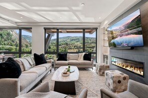 A modern living room with a fireplace, large windows, and a television. - Beaver Creek Penthouse - Luxe Amenities&Mtn Views (Avon)