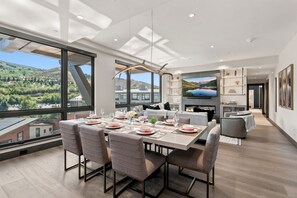 A modern dining area with a large table set for six, a fireplace, and a large window offering a scenic view. - Beaver Creek Penthouse - Luxe Amenities&Mtn Views (Avon)