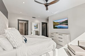 Een moderne slaapkamer met een bed, een televisie, een dressoir en een plafondventilator.