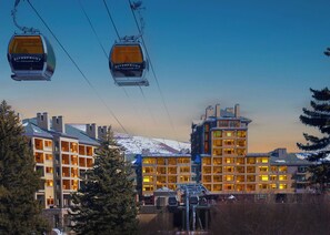 A ski lift with cabins labeled 'Riverfront Village' and a building complex with multiple floors and large windows. - Beaver Creek Penthouse - Luxe Amenities&Mtn Views (Avon)