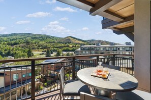Un balcón con una mesa y sillas, con vistas a una zona residencial con edificios y colinas.