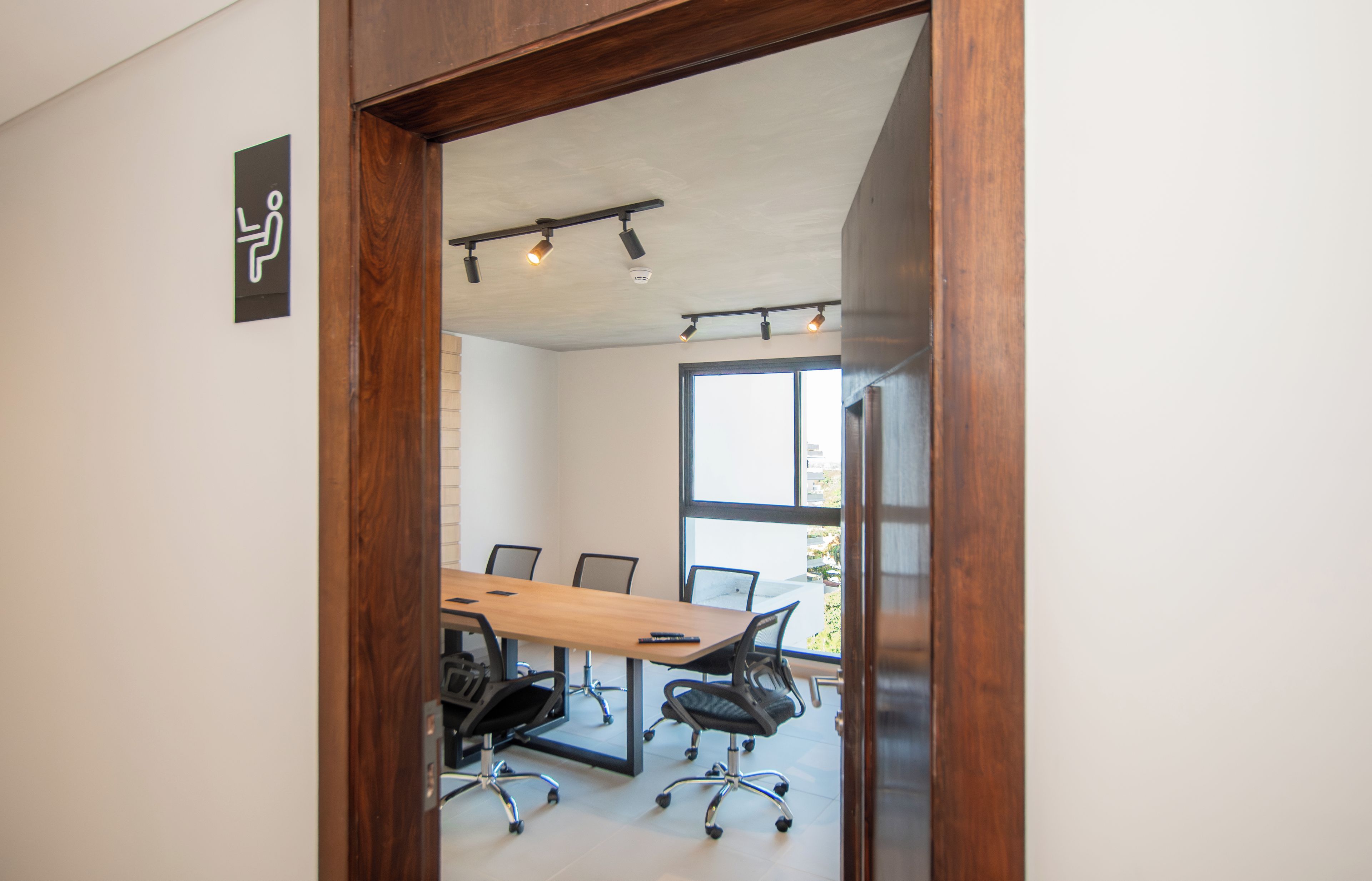 A conference room with a wooden table, black office chairs, and a large window providing natural light.